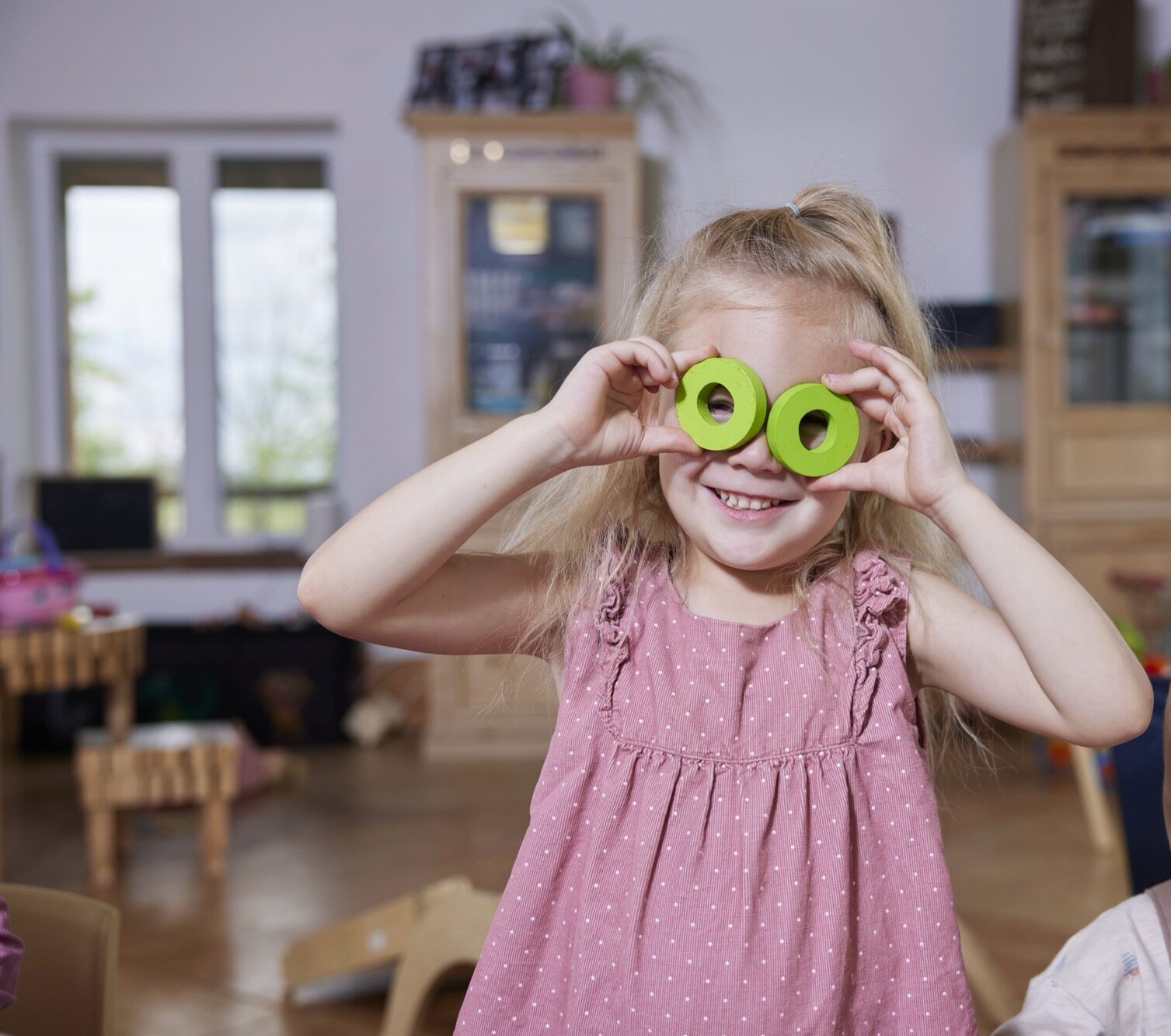 Little girl playing with colourful wooden block in front of her face, holding them as pretend glasses.