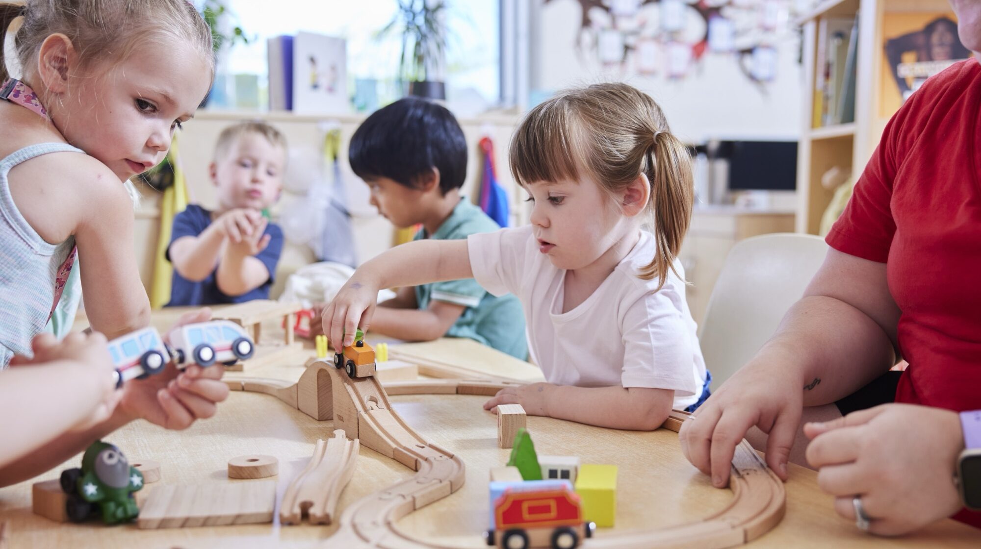 A group of small children playing with wooden cars on a wooden track